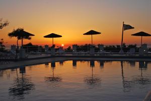 a sunset over a pool with chairs and umbrellas at Santorini Camping & Hostel in Fira