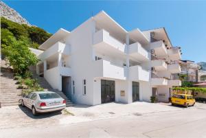 a white building with a car parked in a parking lot at Apartman Mira- Omis in Omiš