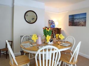 ノリッジにあるDairy Barns Holiday Cottagesのダイニングルームテーブル(白い椅子、黄色い花付)