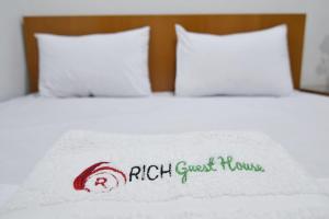 - un lit avec une couverture blanche avec les mots riches de la maison d'hôtes dans l'établissement Rich Guesthouse, à Palmerah