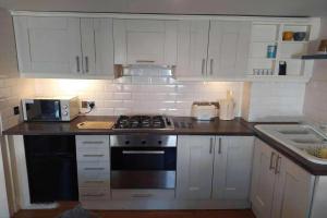 uma cozinha com armários brancos e um forno com placa de fogão em French Horn Cottage em Ware