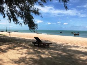 a bench on a beach with boats in the water at Ao Thai Resort in Sathing Phra