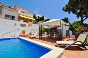 a swimming pool with chairs and an umbrella next to a house at Villa Cala Trons in Lloret de Mar