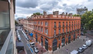 un grand bâtiment en briques rouges dans une rue de la ville dans l'établissement Hotel Ours Blanc - Place Victor Hugo, à Toulouse