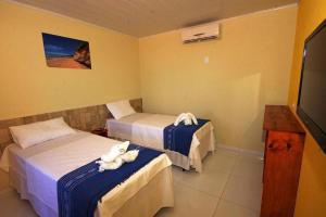 a hotel room with two beds and a television at Pousada Mama Pereira in Japaratinga