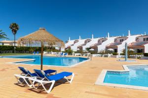 um resort com uma piscina e duas cadeiras e um guarda-sol de palha em Moradias Villas Joinal em Albufeira
