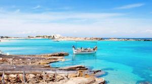 a boat in the water next to a beach at Bonito apartamento a 20m del mar in Es Pujols