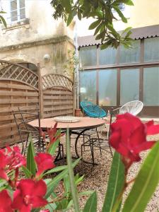 un patio con mesa, sillas y flores rojas en Arles Rental-Côté Forum. en Arlés