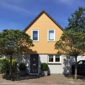 ein gelbes Haus mit zwei Bäumen davor in der Unterkunft Vakantiewoning in villapark de oesterbaai 113 in Wemeldinge
