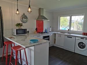 una cocina con electrodomésticos blancos y taburetes rojos en Kerikeri Sunny Modern 2 Bedroom Apartments, en Kerikeri