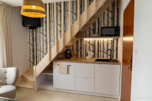 a kitchen with white cabinets and a wooden stair case at Domki Letniskowe AlexJan in Dąbki