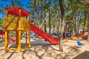 une aire de jeux avec un toboggan rouge et un arbre dans l'établissement Camping Stella Maris Mobile Homes, à Umag