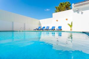 a swimming pool with blue chairs next to a building at Villa Sol e Mar in Charneca