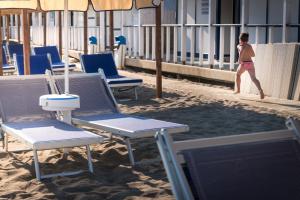 a man walking on the beach with chairs and umbrellas at Hotel Perla in Castiglione della Pescaia