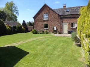 une maison en briques avec une grande pelouse devant elle dans l'établissement Lapwing Cottage, à Stoke-on-Trent