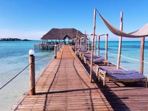 a wooden pier with chairs and a house on the water at Reef & Beach Resort - Spa Jambiani in Jambiani