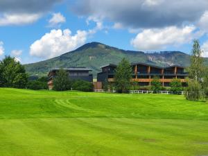 a building on a green field with a mountain in the background at Green apartmány in Čeladná