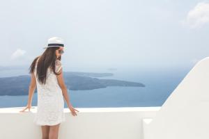 Una mujer con un vestido blanco y sombrero mirando hacia el agua en Agave Santorini Design Boutique Hotel, en Imerovigli