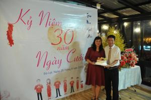 Ein Mann und eine Frau stehen vor einem Schild mit einem Kuchen in der Unterkunft Anh Trang Homestay in Da Lat