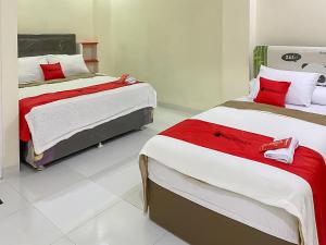 two beds in a room with red and white sheets at RedDoorz Syariah near PKOR Lampung in Bandar Lampung