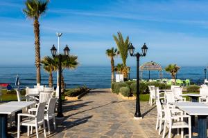 a row of tables and chairs with the ocean in the background at Kefalos Beach Tourist Village in Paphos City