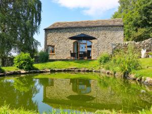 ein Cottage aus Stein mit einem Sonnenschirm über einem Teich in der Unterkunft The Barn in Harrogate