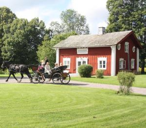 uma carruagem puxada por cavalos em frente a um celeiro vermelho em B&B Kvarntorps Herrgård em Forshaga