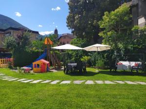 einen Garten mit Tischen und Sonnenschirmen und einem Spielplatz in der Unterkunft Palazzo Pellanda in Domodossola