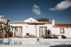 a house with a swimming pool and an umbrella at Casa dos Junqueiros - Countryside Guest House in Caldas da Rainha