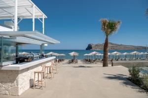 a beach with chairs and a palm tree and the ocean at Sea Front Suites, Maisonettes & Apartments in Agia Marina Nea Kydonias