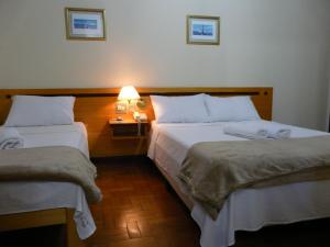 um quarto de hotel com duas camas e uma mesa com um candeeiro em HOTEL VARGINHA em Varginha