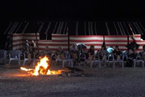 um grupo de pessoas sentadas à volta de uma fogueira na praia em Wadi Ghwere Camp مخيم وادي الغوير em Al Khuraybah
