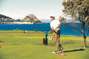 a man standing on a golf course with a castle in the background at Beachcombers Hotel in Saint Helier Jersey