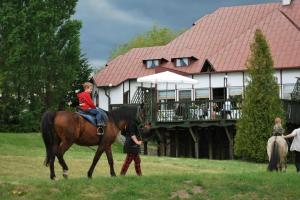 a child riding a horse in front of a house at Jabłoniowy Dworek Kociewie in Malenin