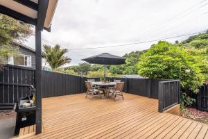 una terraza de madera con mesa y sombrilla en La Petite Maison - Akaroa Holiday Home en Akaroa