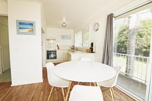 a white kitchen with a white table and chairs at Beachcomber - Pet Friendly in Merimbula