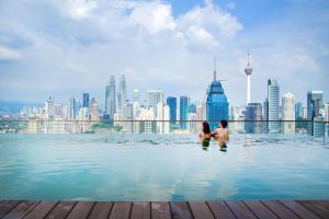 クアラルンプールにあるRegalia Suites Infinity Pool Kuala Lumpurの街のスカイラインを眺めながらインフィニティプールに座っているカップル