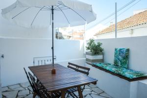 una mesa de madera y sillas con una sombrilla en el balcón en Casa das Aguarelas - Apartamentos, en Ericeira
