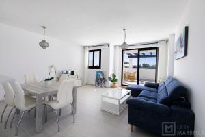 uma sala de estar com uma mesa e um sofá azul em Estepona Sunsets - Modern 3-BR Beachside Apartment em Estepona