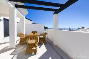 een patio met rieten stoelen en een tafel op een balkon bij Estepona Sunsets - Modern 3-BR Beachside Apartment in Estepona