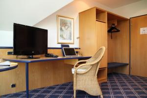 um quarto com uma secretária, uma televisão e uma cadeira em Hotel Zur Post em Ismaning