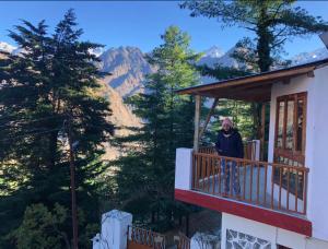 a man standing on a balcony of a house at Resort With Mesmerizing Mountain Views & Pine Trees in Joshīmath