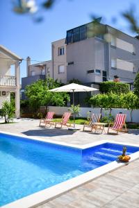 uma piscina com cadeiras e um guarda-sol e um edifício em Pool house LUKA em Zadar