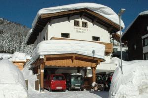 a building covered in snow with cars parked in front at gästehaus stadle in Sankt Anton am Arlberg