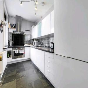 a kitchen with white cabinets and black counter tops at Highgate Maisonette with Roof Terrace in London