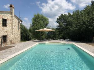 a swimming pool in front of a building with an umbrella at Beautiful Stone Country Villa in Casaprota