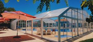 a glass building with a pool and a table and an umbrella at Camping Villa Park Zambujeira do Mar in Zambujeira do Mar
