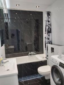 Baño de azulejos negros con aseo y lavamanos en Przymorze Spectrum Apartment for you z halą garażową, en Gdansk
