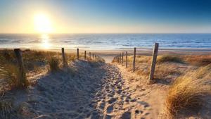 a sandy path to the beach with the sun in the background at Gastenverblijf De Ruyter in Koudekerke