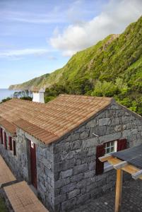 Casa de piedra con techo de baldosa y montaña en Casas Da Faja en Praia do Norte
